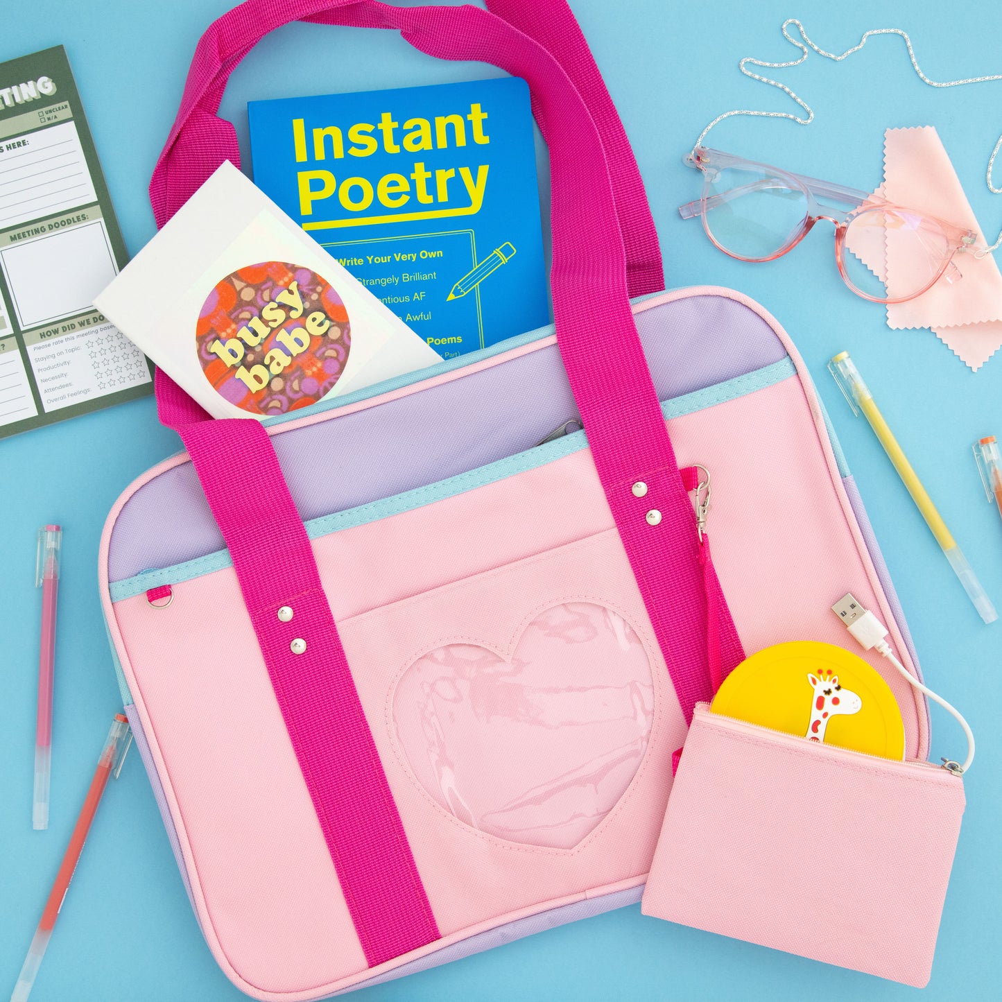 A collection of items from The Oddball Club includes an instant poetry book, pink glasses, a laptop bag with a clear heart and pink straps, busy babe notebook, and gel pens.
