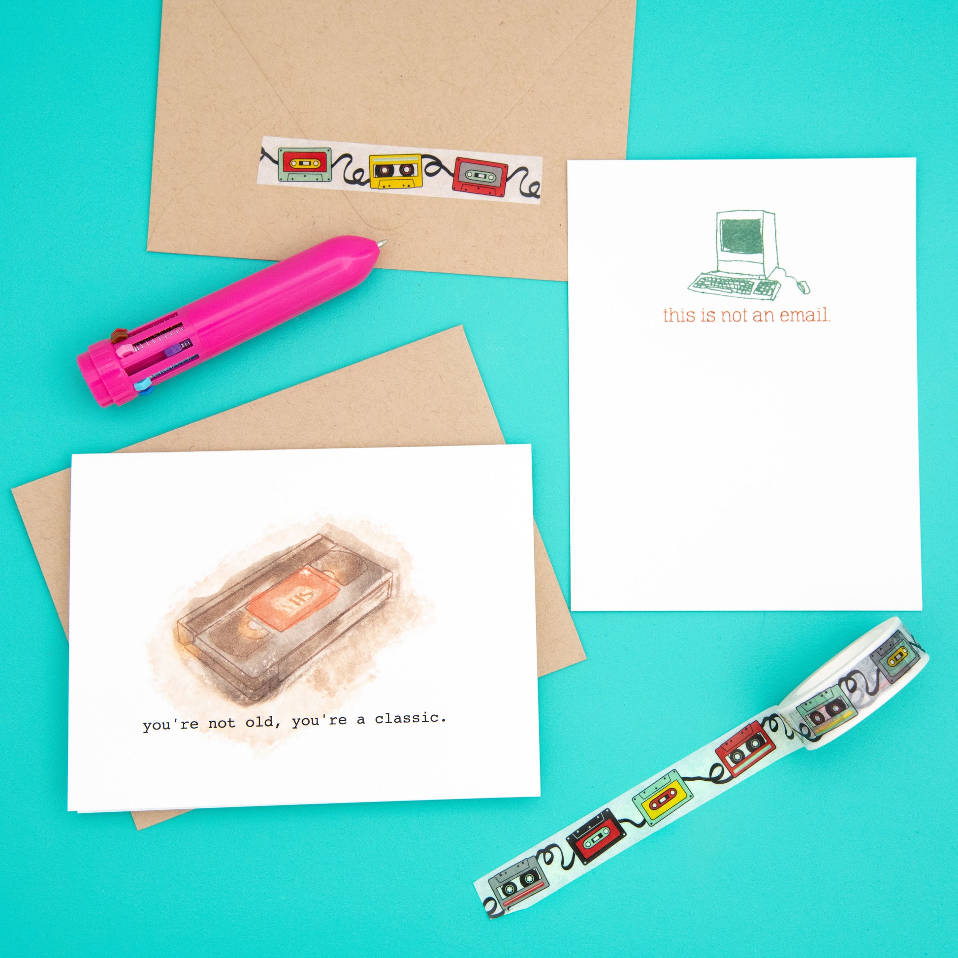 A retro-themed stationery set featuring a VHS tape greeting card, tape-shaped washi tape, 'Not an Email' flat note card, pen, and envelope. Perfect for those who appreciate unique and quirky paper goods from Ratbone Skinny.