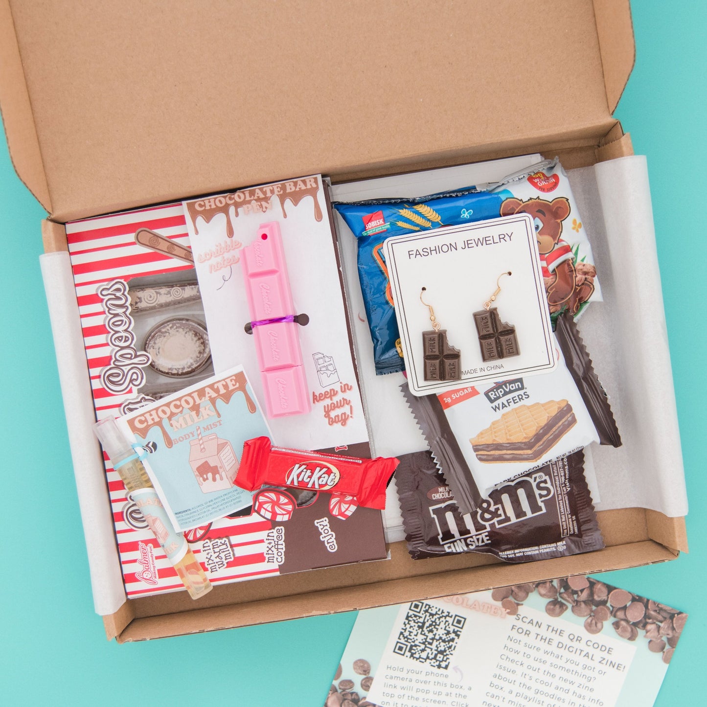 Indulge in our chocolate-themed subscription box! Includes a holiday greeting card, delicious snacks, chocolate spoons, and novelty earrings and pen.