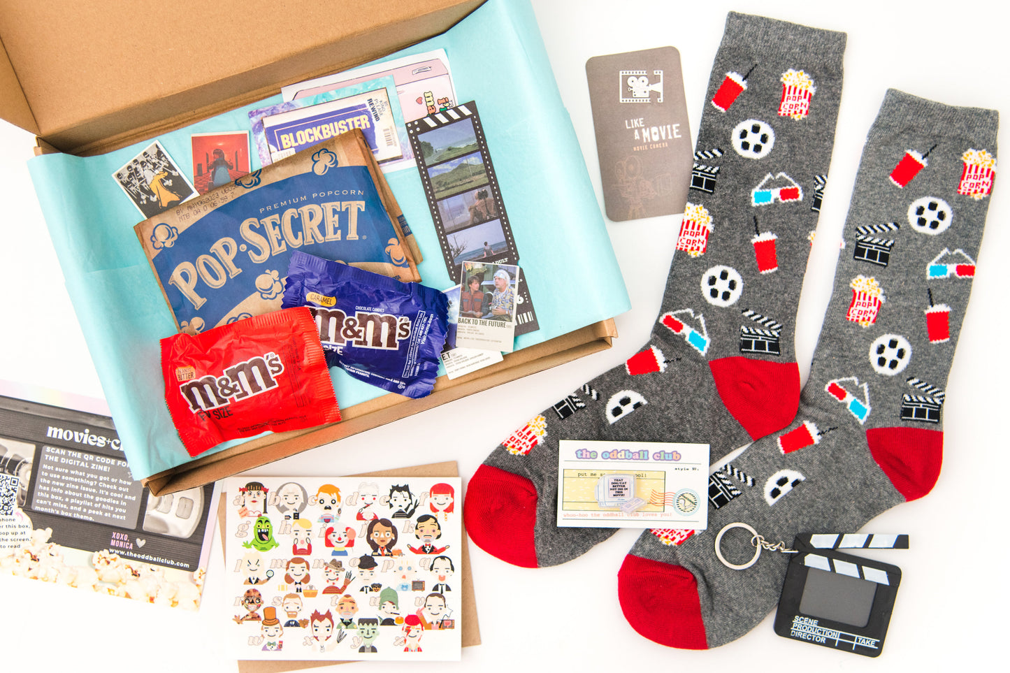 A movie-themed subscription box open with film reel socks, movie art greeting card, TV pin, clip board keychain, and popcorn. Get your film fix with Oddball Club's curated selection of cinema-inspired accessories and collectibles.