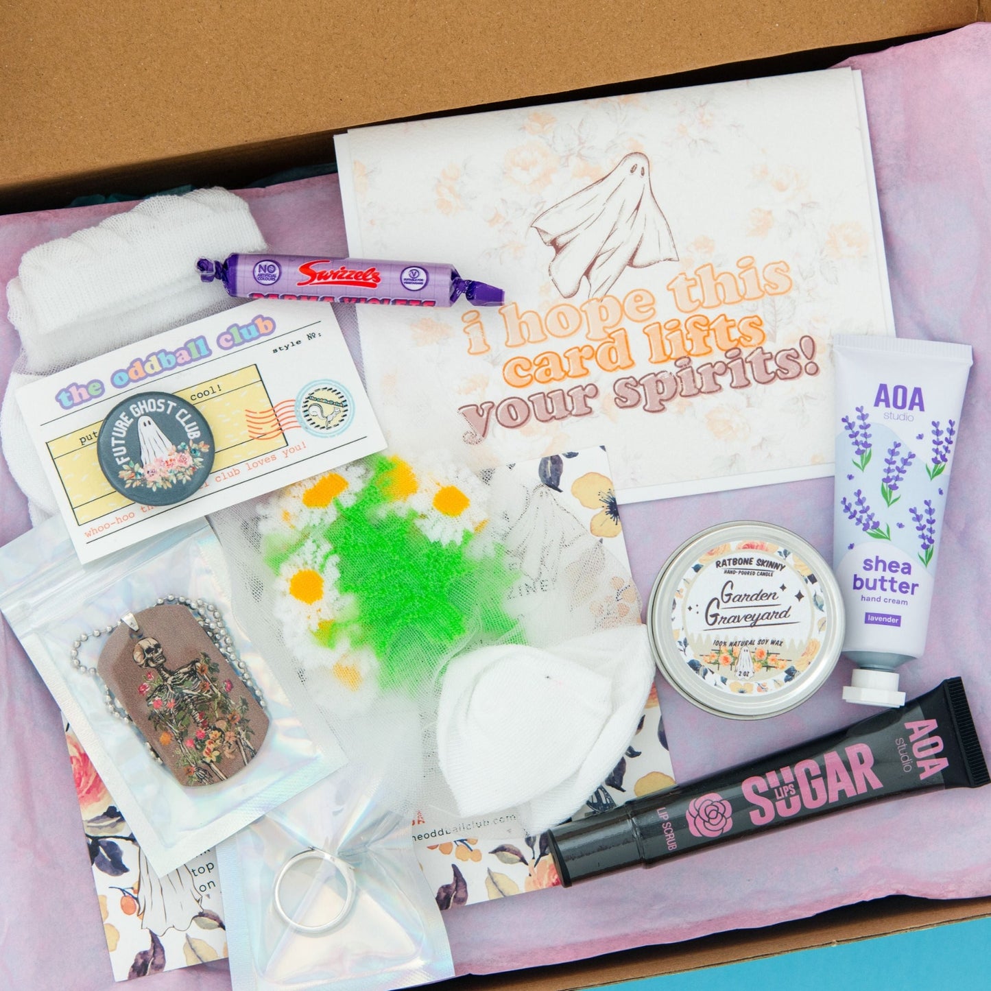 Unbox a spooky surprise with our ghost-themed subscription box. This set includes a ghost greeting card, sugar lip scrub, a future ghost pin, and a floral skeleton necklace. Also included are a mini candle, tube of hand lotion, a ring, and sheer daisy flower socks. All nestled in purple tissue paper with a floral background, this Halloween box is the perfect treat for any ghost lover.