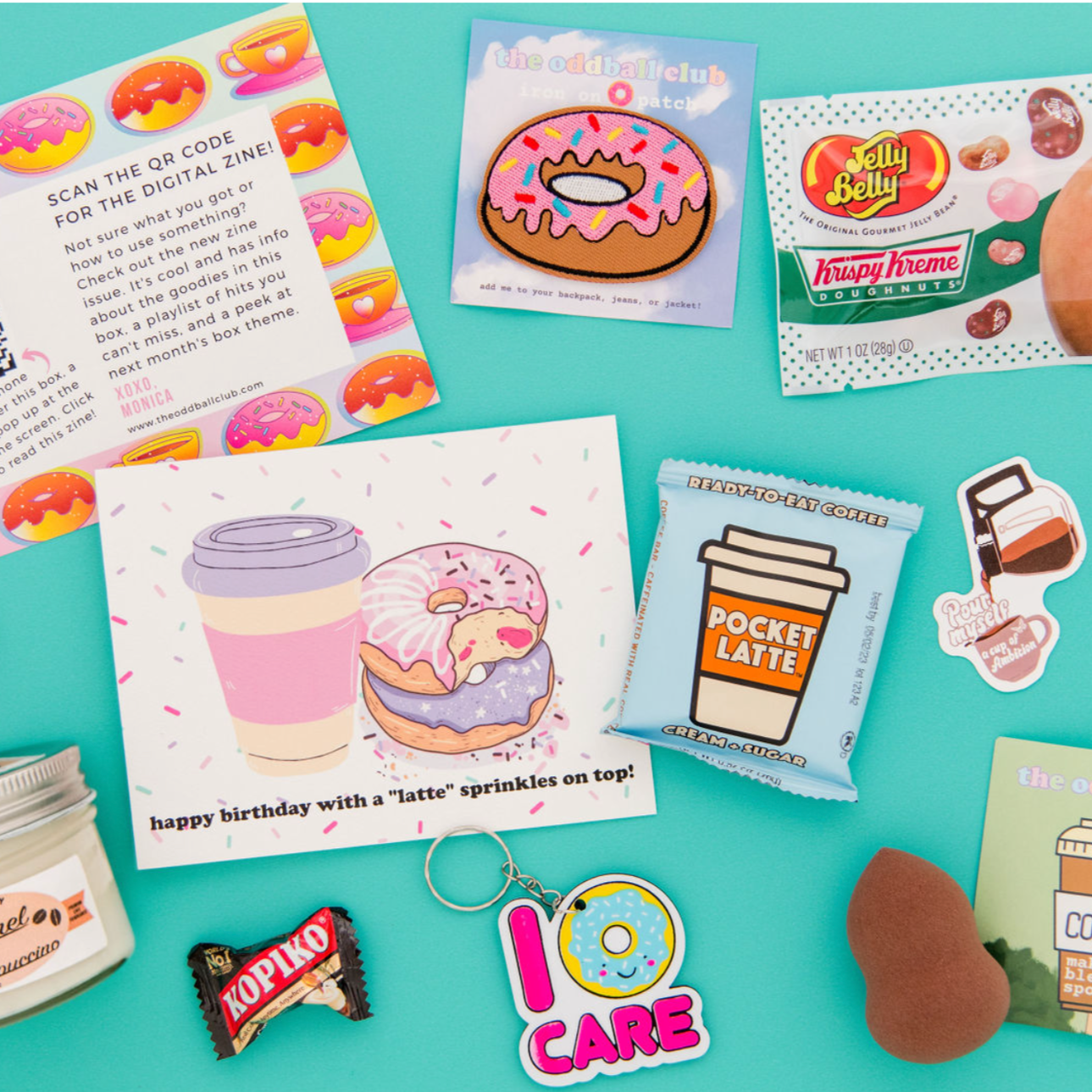 Image of a donut patch and flavored jelly beans, pocket latte chocolate, donut and coffee greeting card, I donut care key chain, Kopiko candy, and a makeup sponge on a blue background. This subscription box is perfect for donut and coffee lovers. Get your sweet fix with our tasty treats and cute accessories. Order now and enjoy your monthly surprise from our team at The Oddball Club.