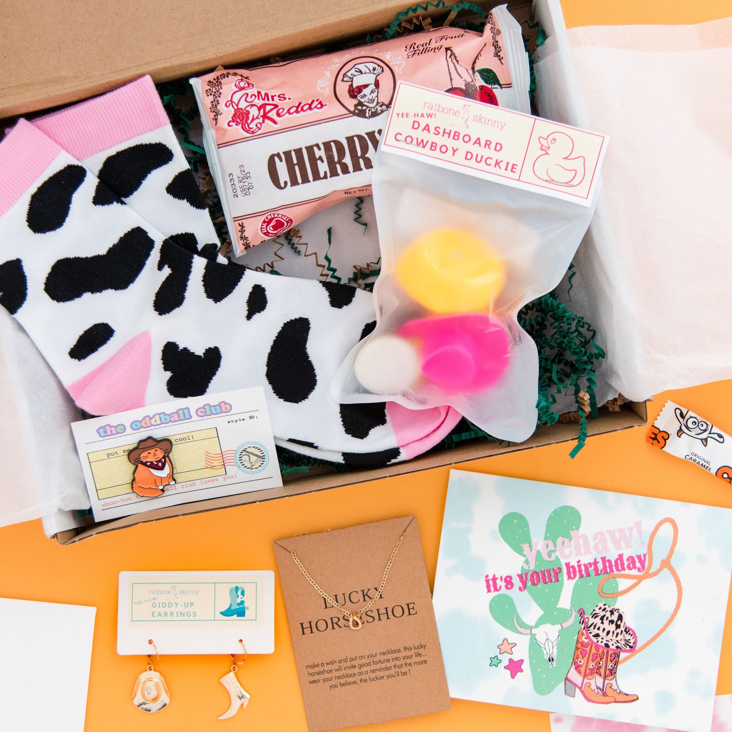 Get your cowboy on with our western-themed subscription box! Featuring a dashboard duckie for your car, a yeehaw greeting card, cow boy hat earrings, lucky horshoe necklace, and cat with bandana and cowboy hat enamel pin. Perfect for those who love all things western and want to add some country charm to their life.