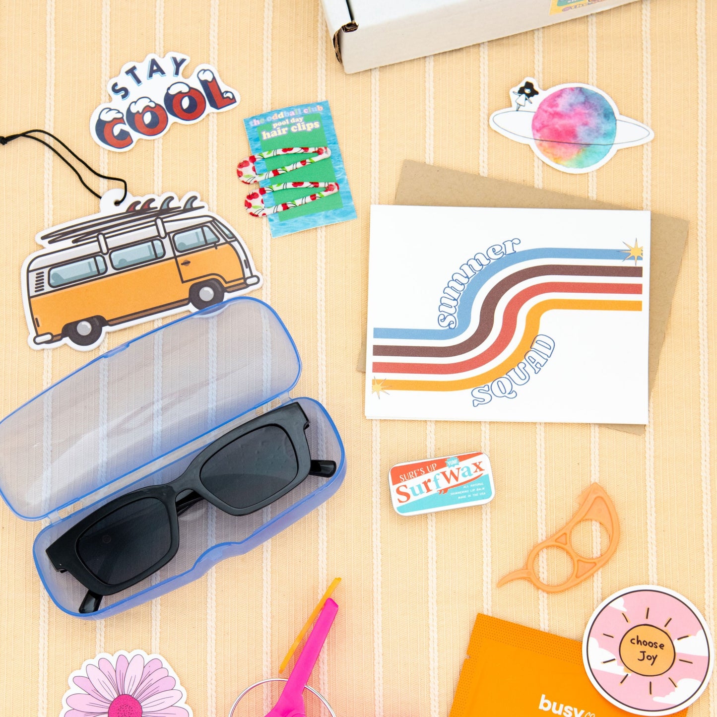 Unleash your inner surfer with this summer subscription box including sunglasses, surf wax chapstick, greeting card, surf wax lip balm tin, orange peeler, stay cool sticker, and surf van air freshener.